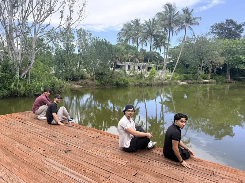 Four Telora fellows sitting on a wooden dock over a pond lined with palm trees