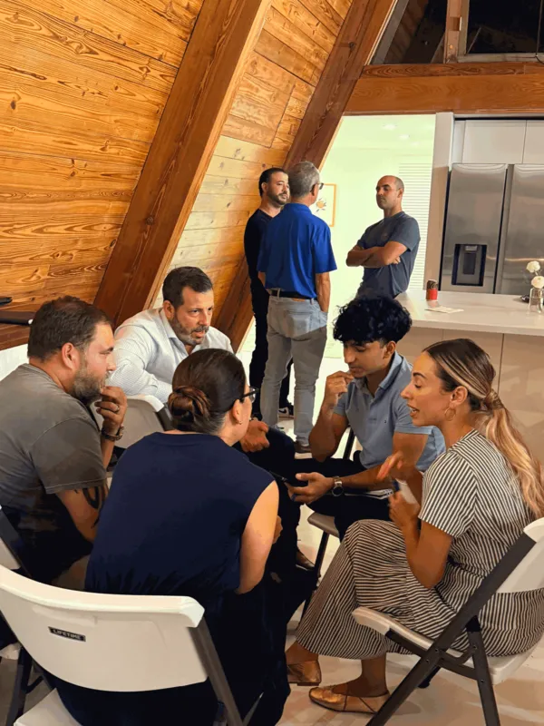 Malik, seated in a circle of people in an A-frame kitchen, shows them Glutt on his phone